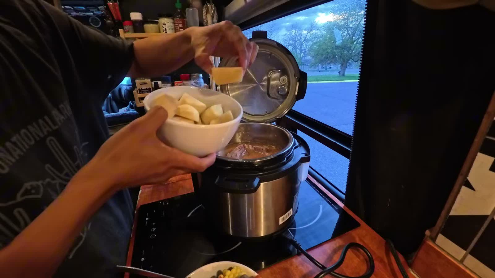 Michael adding a bowl of cut potatoes and a pork bone into the open pressure cooker in the van