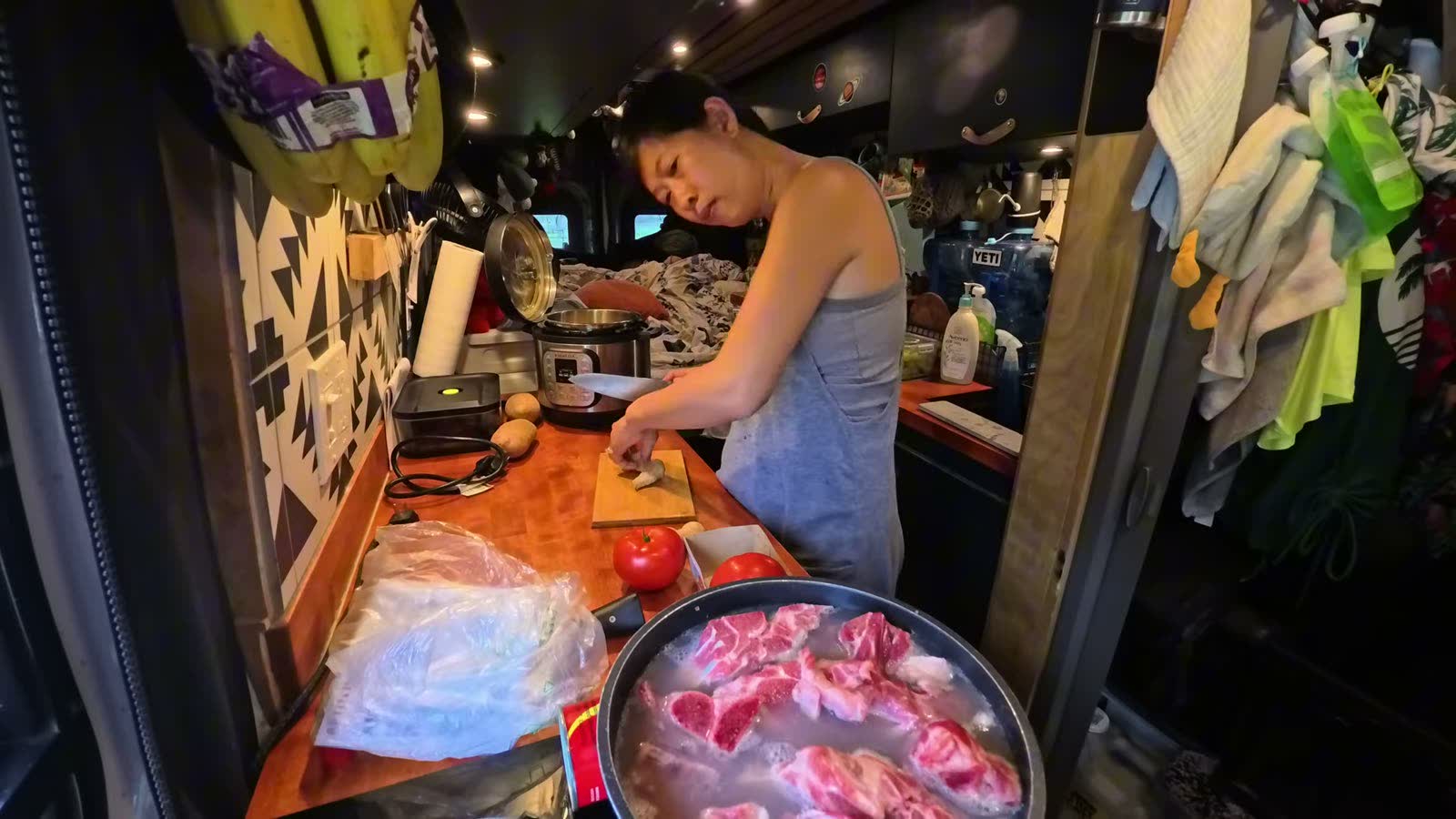 Rina cutting meat at the counter while the pork neck bones blanch in a pot on the induction cooktop