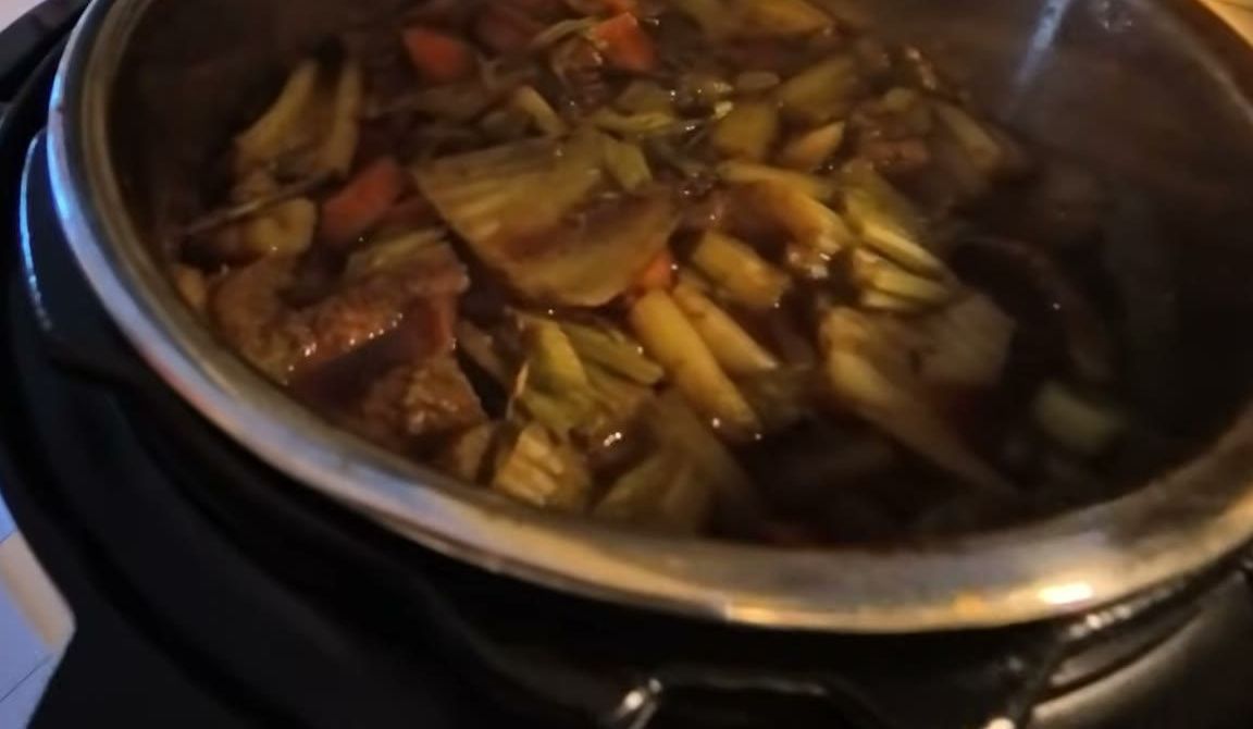 Onions, carrots, celery and herbs cooking in beef stock in a pressure cooker