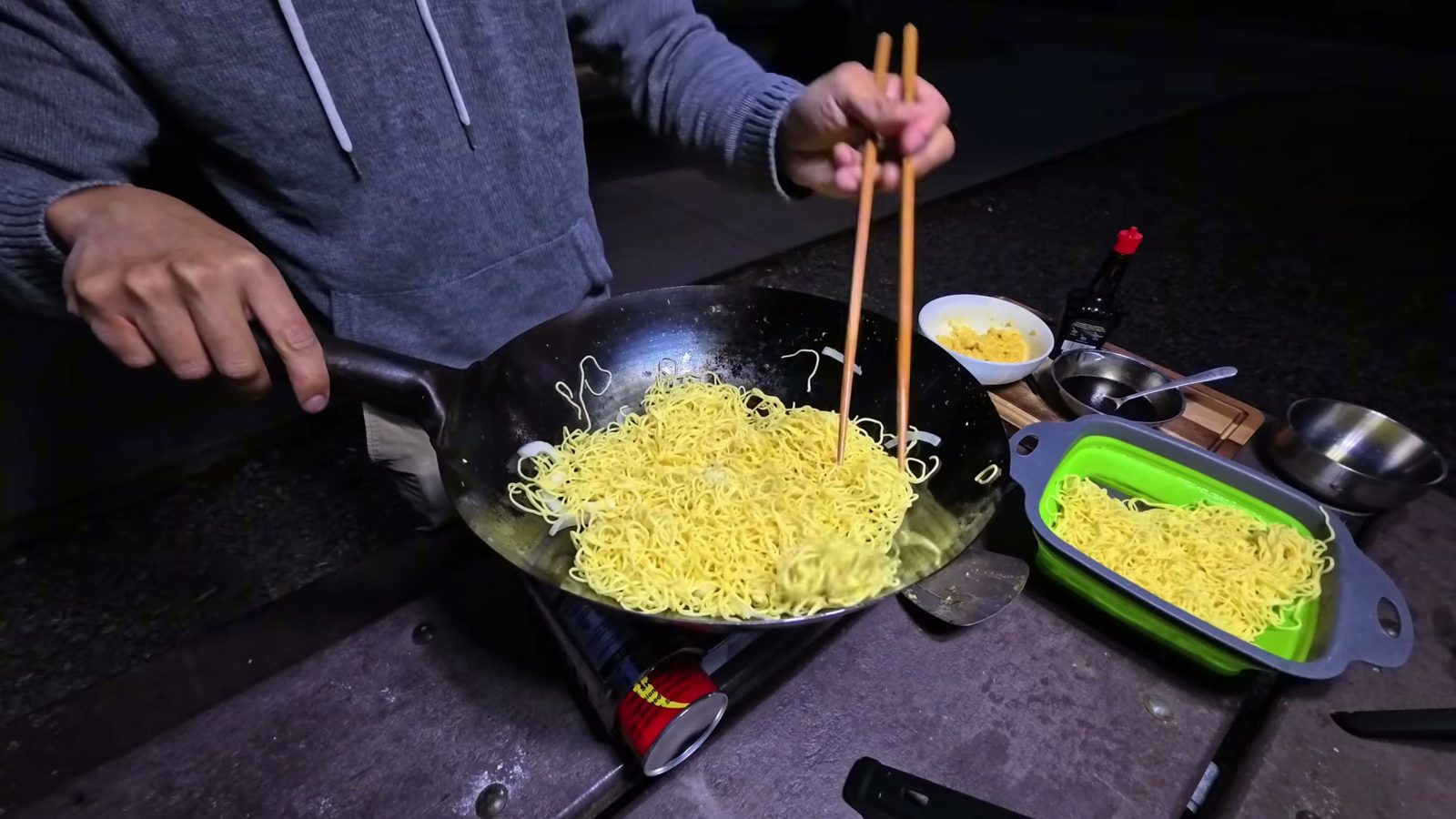 Pan-frying egg noodles in a wok with chopsticks on a butane stove at the campsite