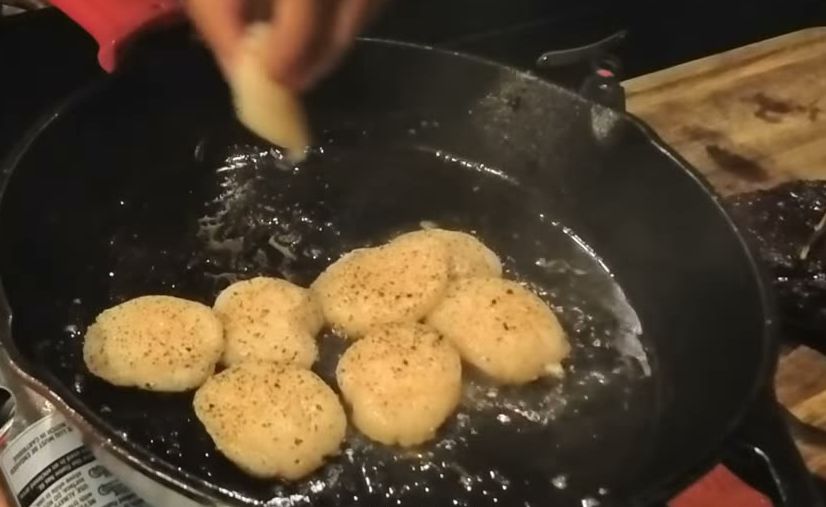 Scallops seasoned with salt and pepper searing in a cast iron pan as butter goes in