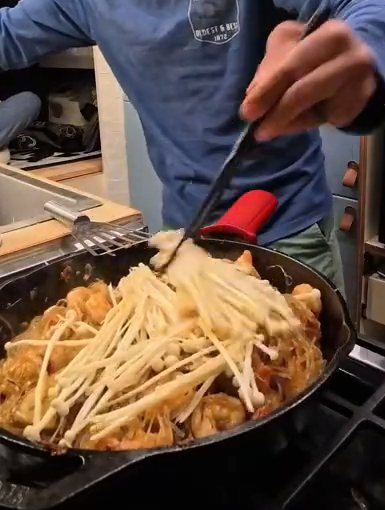 Adding enoki mushrooms on top of the XO vermicelli and shrimp in the cast iron