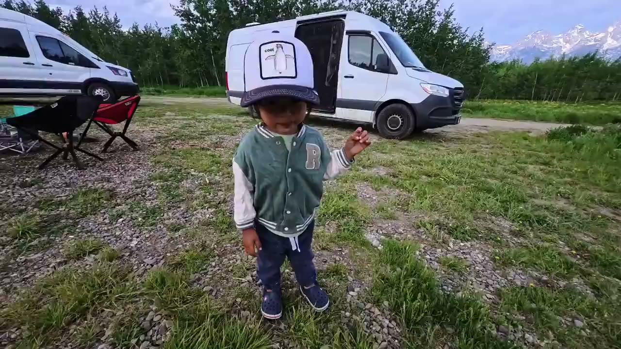 Spencer at a campsite with our van and the mountains behind