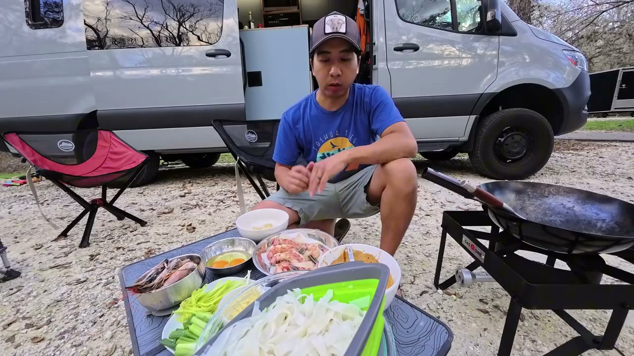 Michael cooking with a wok outside our Sprinter van at a campsite